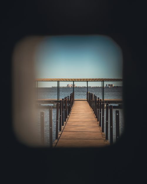 Free Dramatic perspective of a pier through a circular opening amidst calm waters under a clear sky. Stock Photo