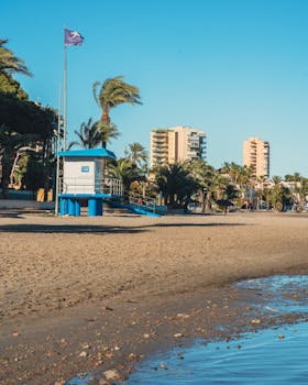 Sandy beach in Santiago de la Ribera, Spain with lifeguard tower and palm trees on a sunny day.