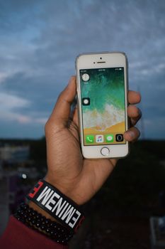 Hand holding a smartphone against a twilight sky, showcasing screen and bracelets.