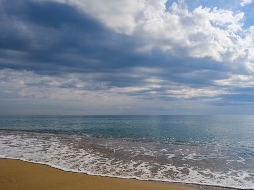 Free Tranquil sandy beach with calming ocean waves beneath a dramatic cloudy sky. Stock Photo