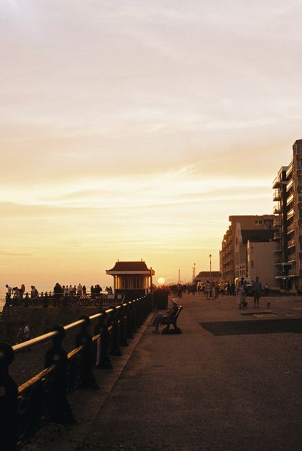People enjoying a sunset walk along an English coastal promenade with buildings in the background.