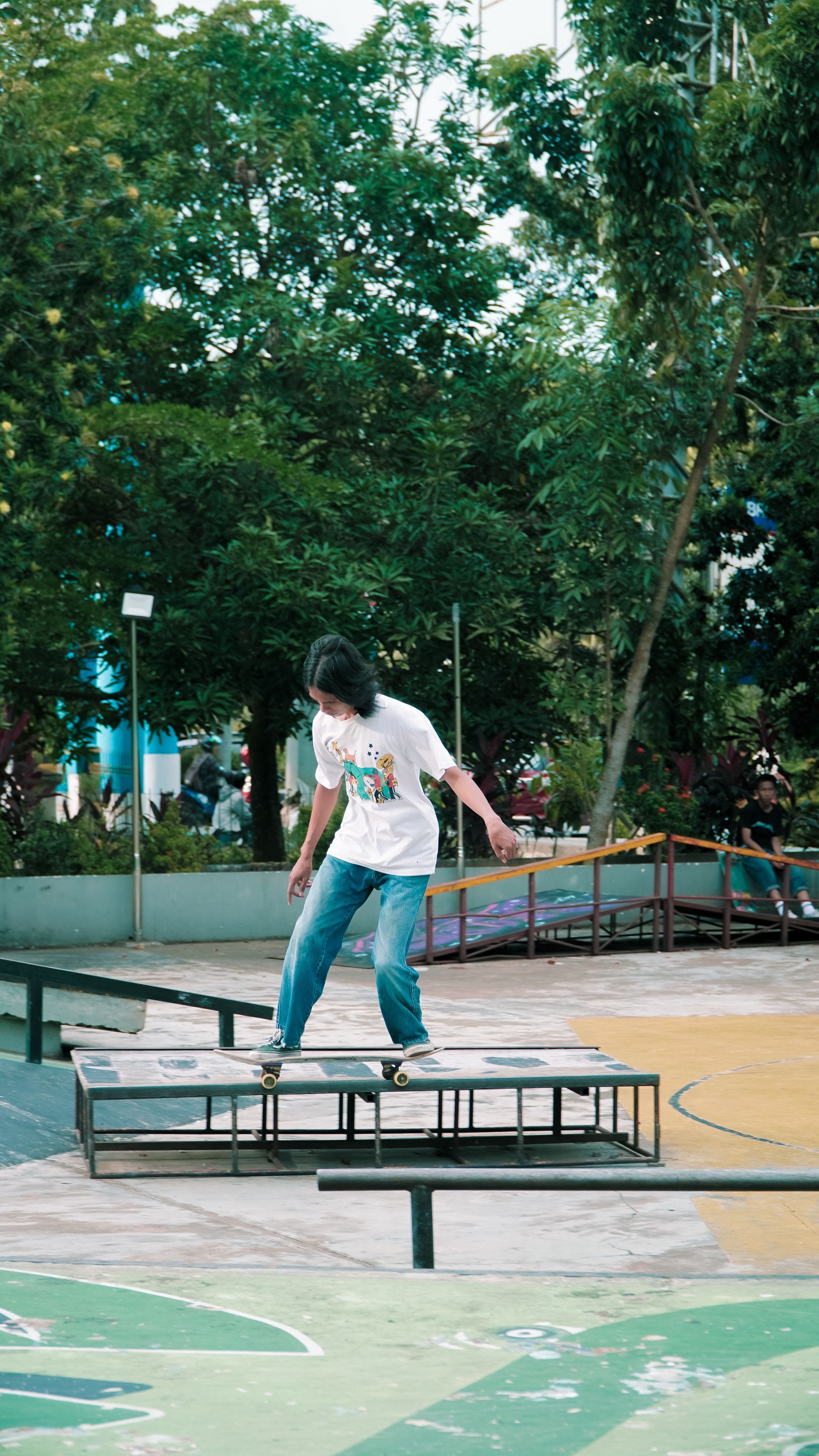 A young woman skateboards on a ramp in an outdoor skate park surrounded by greenery.