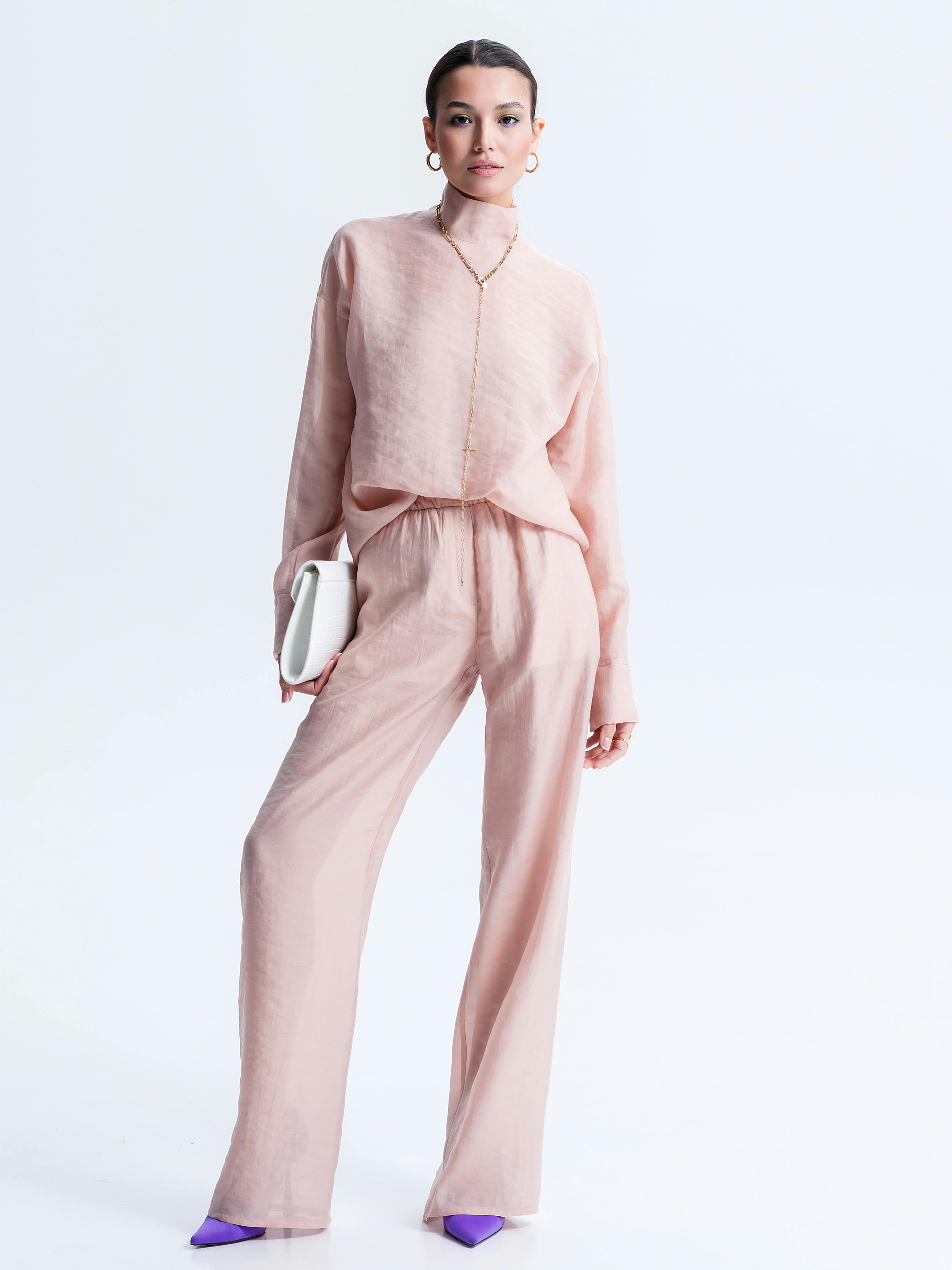 Stylish woman posing in a pastel pink outfit in a bright studio setting.