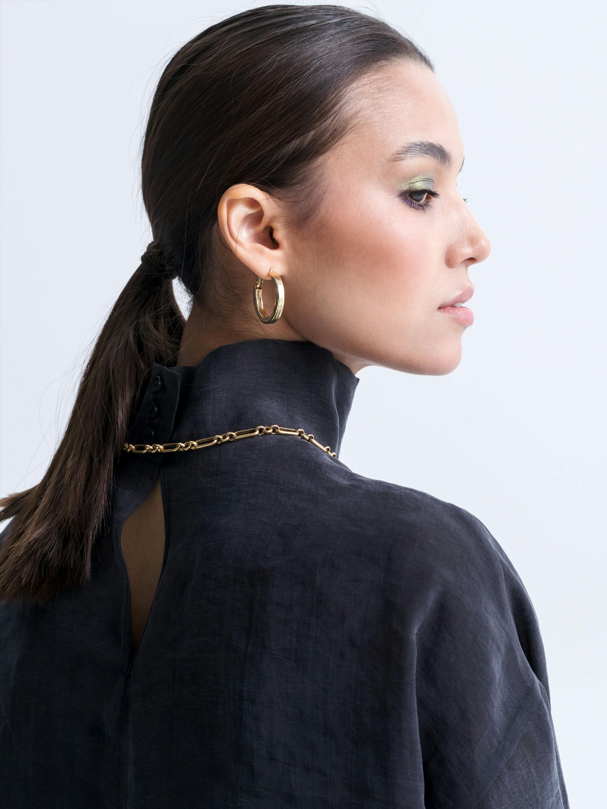 Stylish side profile portrait of a woman in black knitwear with gold jewelry.