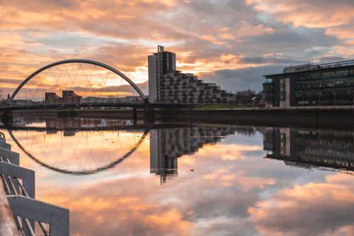 Free Stunning view of Glasgow's Clyde Arc reflecting in the River Clyde at sunset with modern architecture. Stock Photo