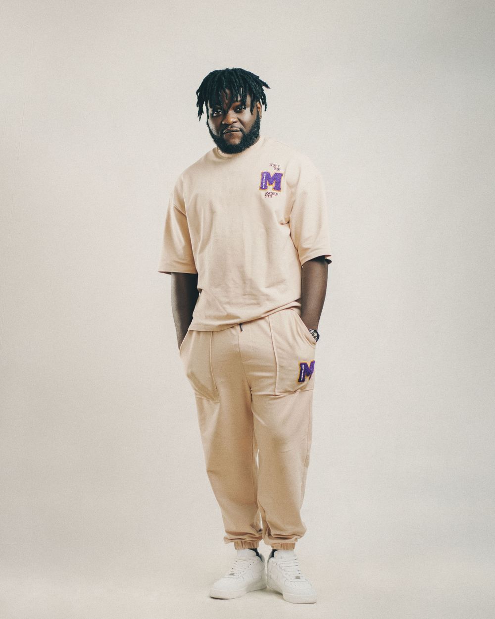 Man wearing a simple beige T-shirt and trousers with white sneakers in a studio