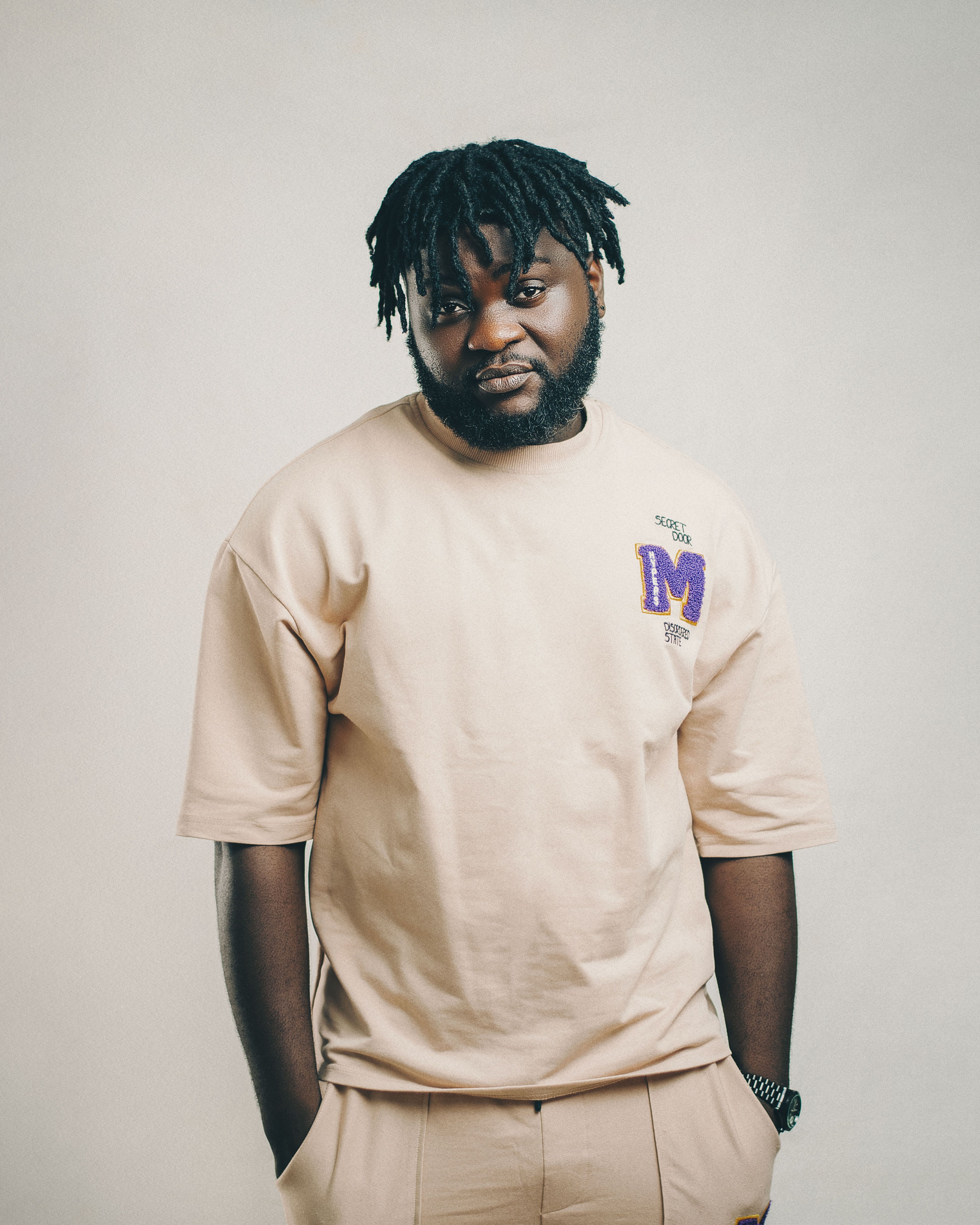 Portrait of a fashionable man with dreadlocks posing confidently in a studio setting.