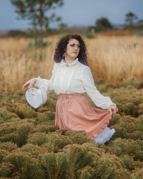 Curly Woman in White Blouse and Pink Skirt Standing in a Field