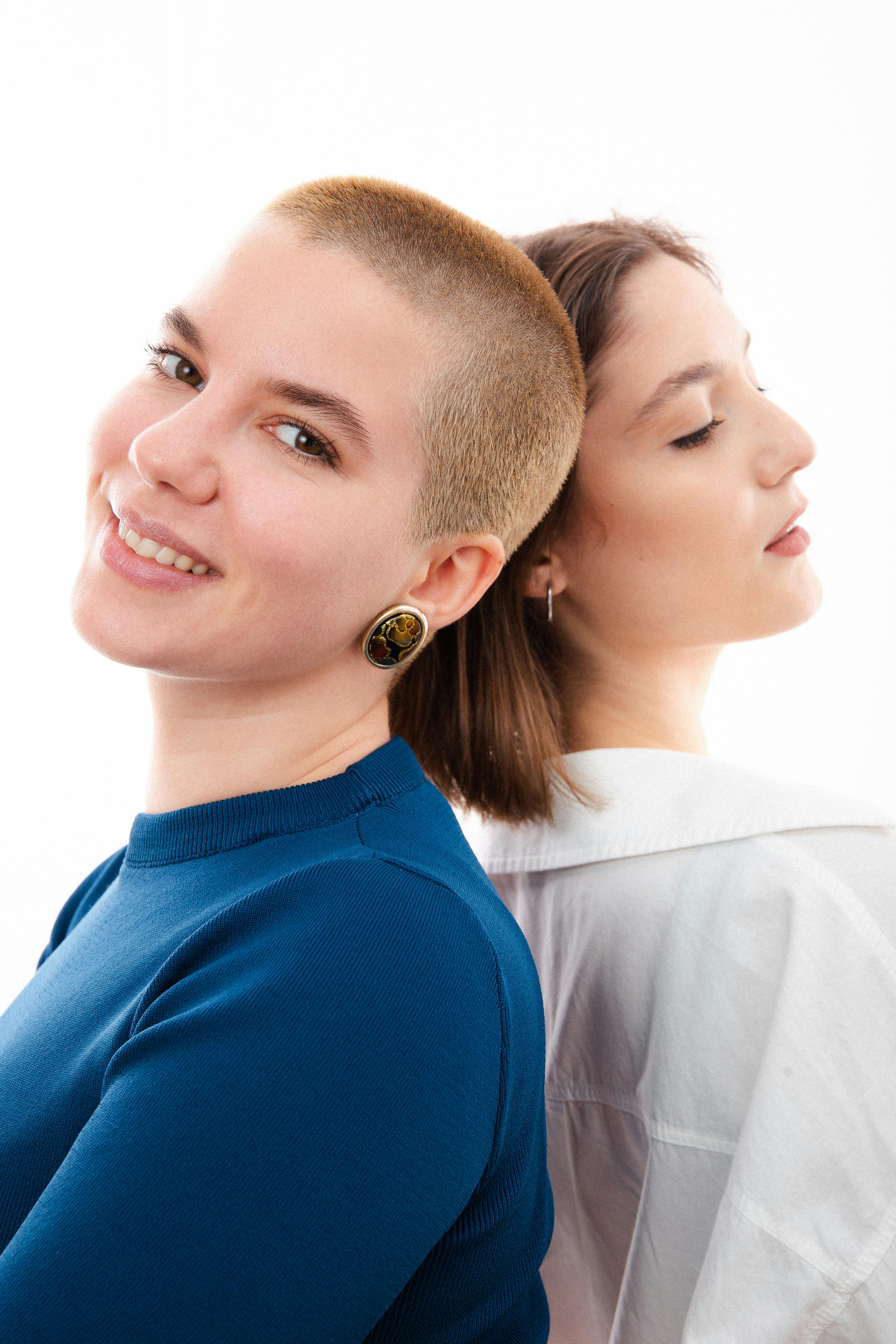 Two diverse women standing back to back, smiling against a white background in a studio shoot.