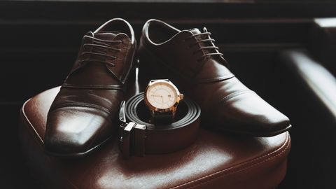 Close-up of stylish men's shoes, belt, and wristwatch on a leather chair, showcasing elegance and fashion.