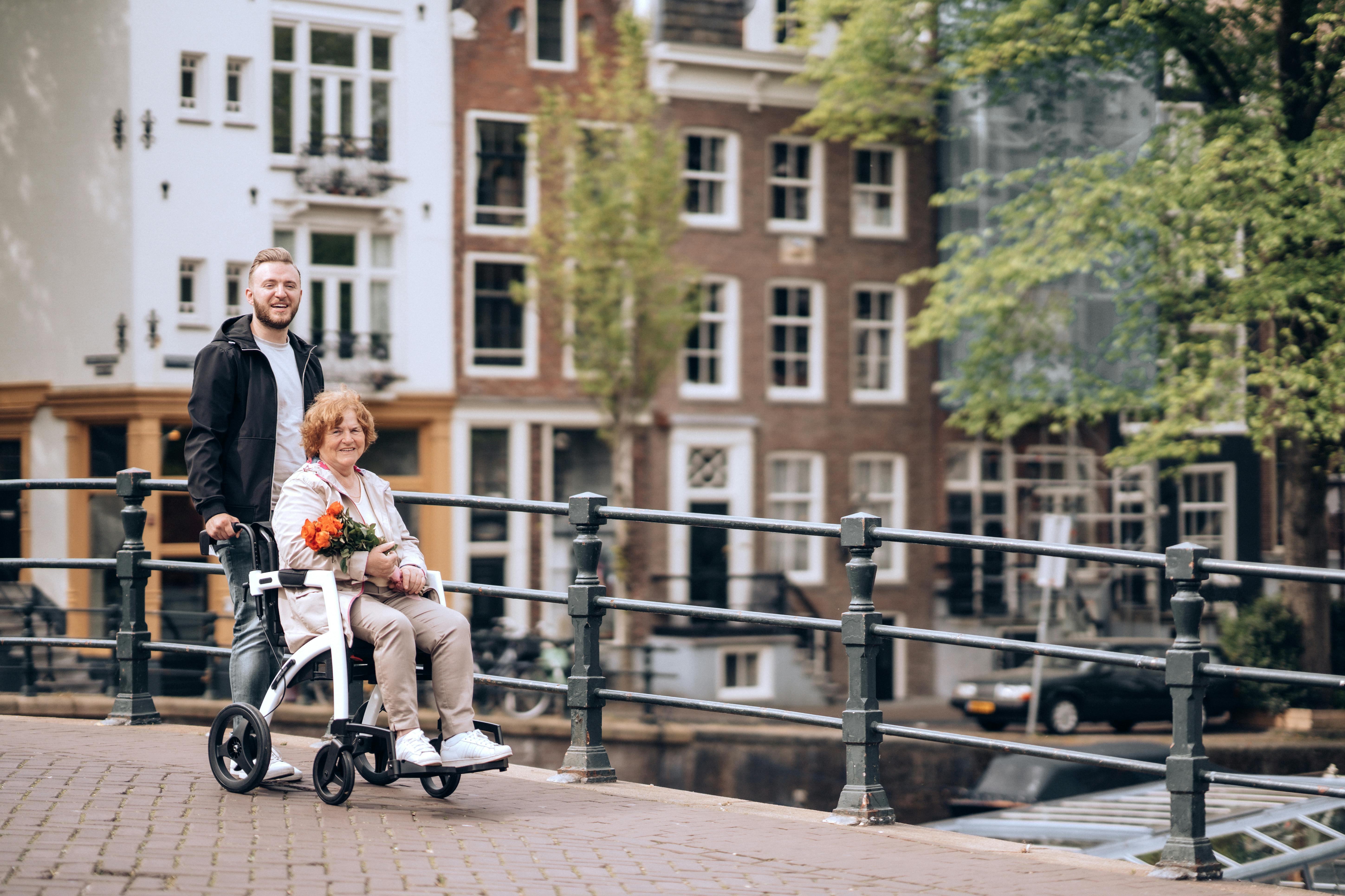 Free A senior woman in a wheelchair with flowers enjoys a stroll along Amsterdam's iconic canals. Stock Photo
