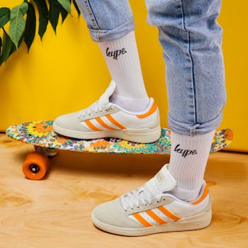 Close-up of stylish sneakers with vibrant skateboard against a yellow backdrop.