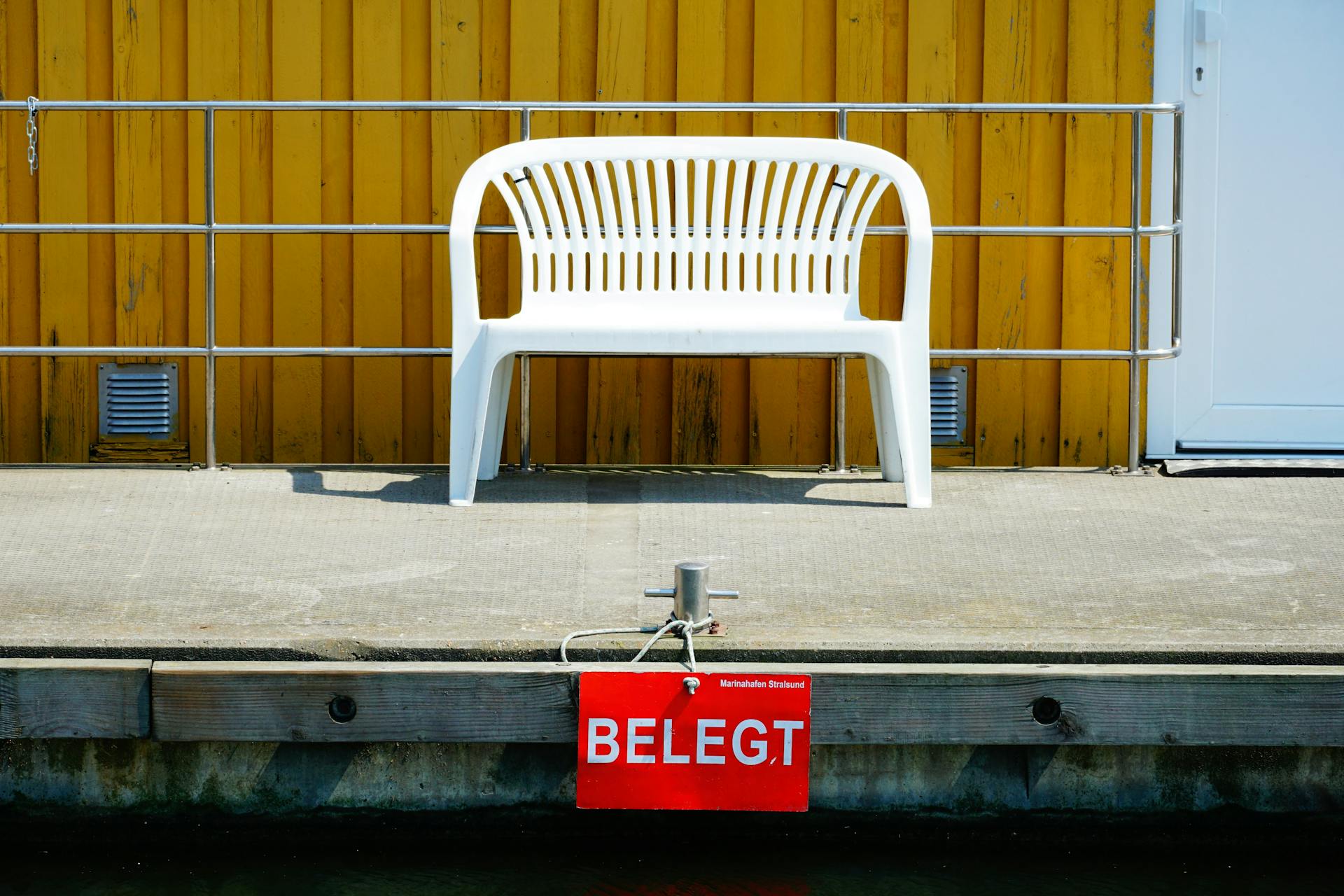 Minimalist outdoor scene with a white plastic bench, yellow wall, and reserved sign.