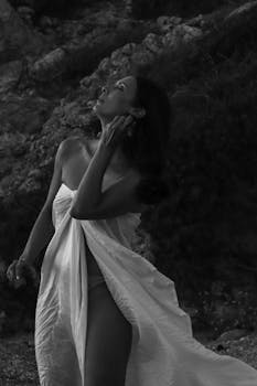 Artistic black and white portrait of a woman posing elegantly on a rocky beach.