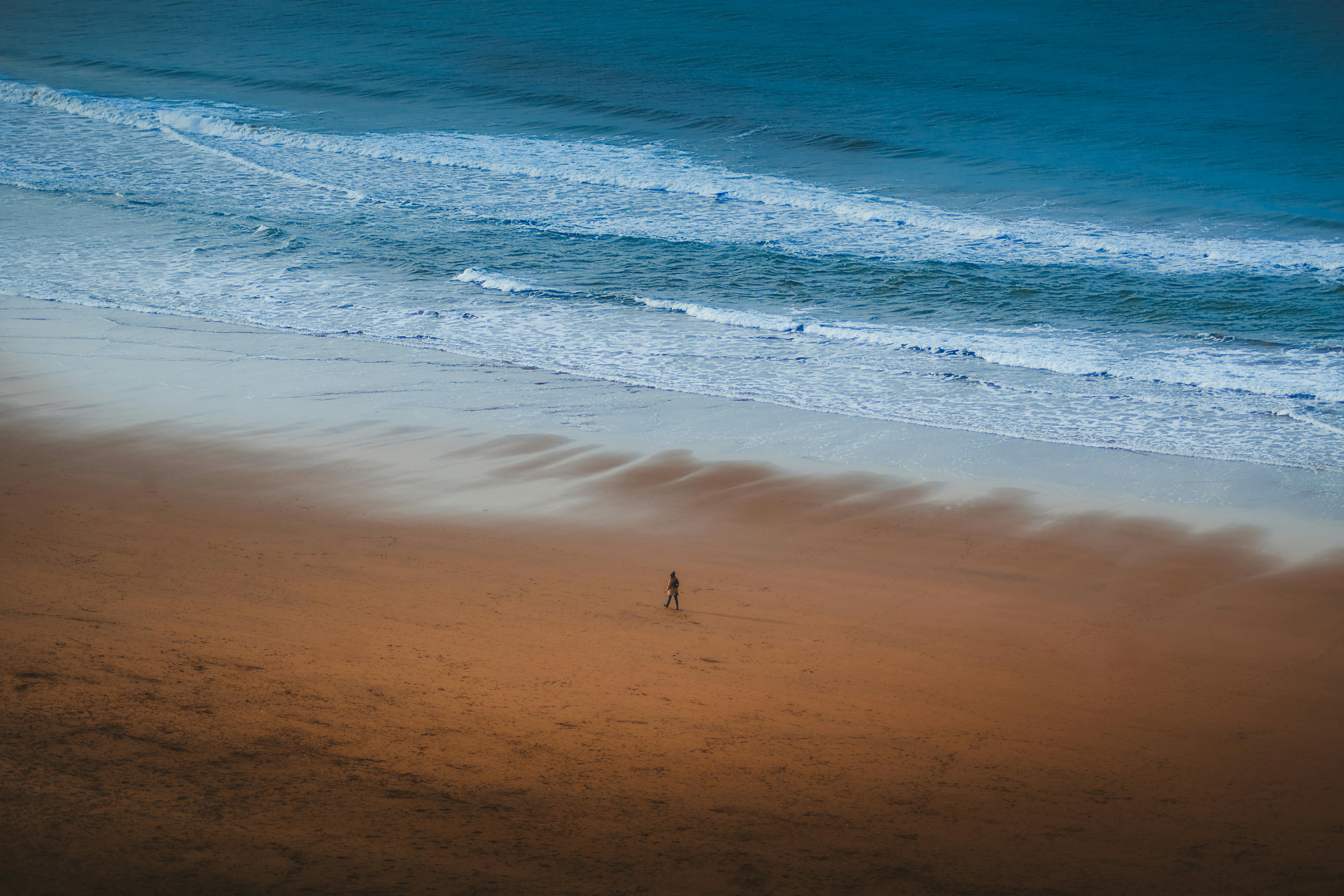 Aerial view of a solitary person walking along the sandy beach with waves in Bilbao, Spain.