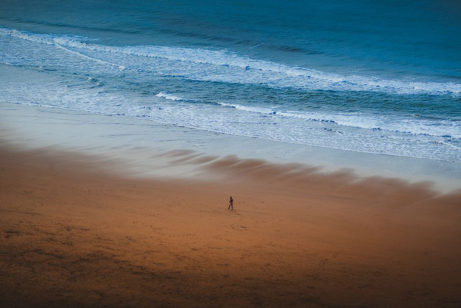 Aerial view of a solitary person walking along the sandy beach with waves in Bilbao, Spain.