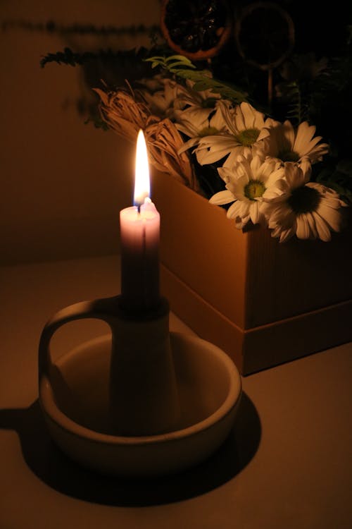 Close-up of a Burning Candlestick Standing next to Flowers 