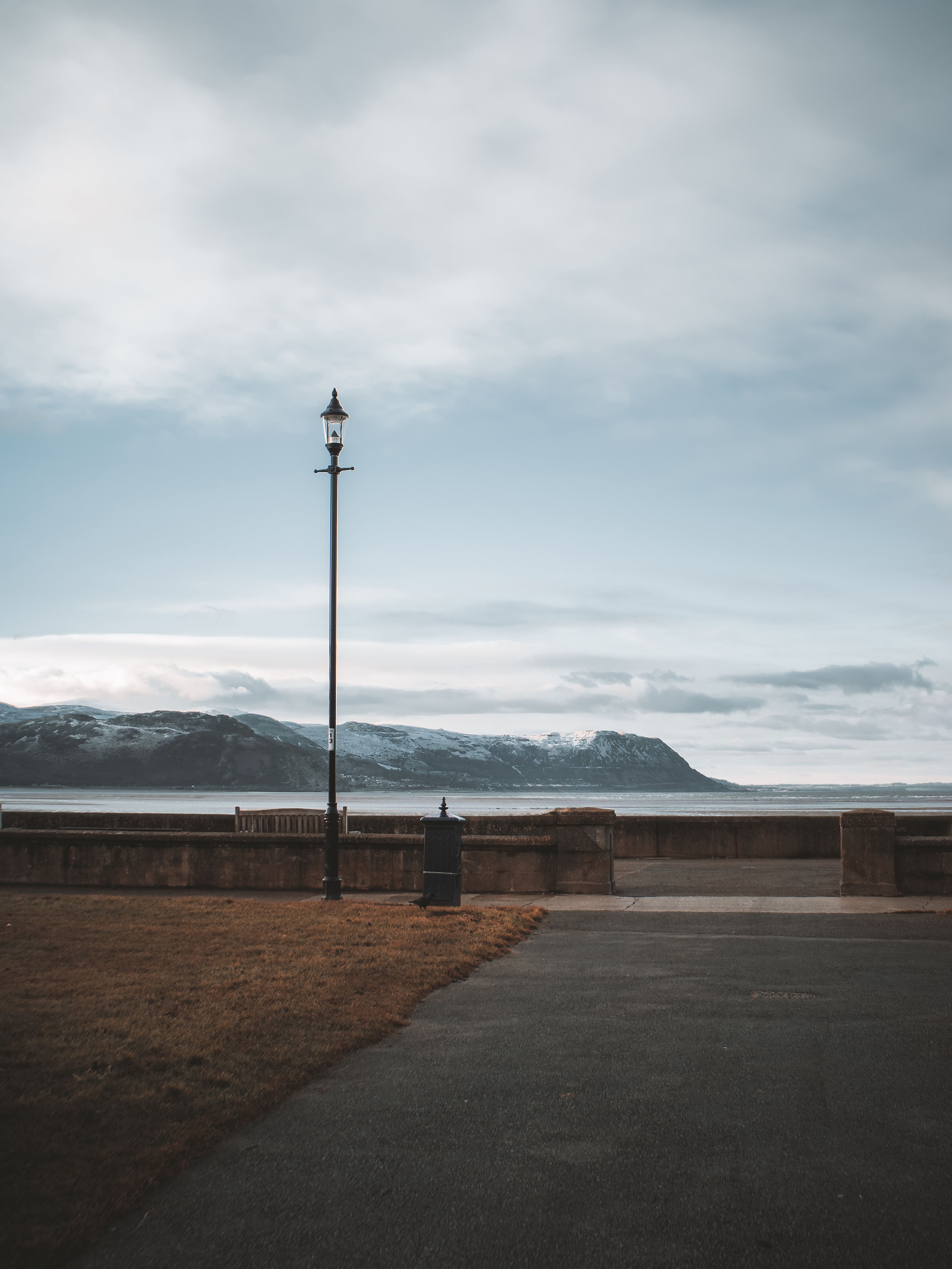 A serene view of a seaside promenade in Llandudno, Wales featuring a lamppost and distant mountains.