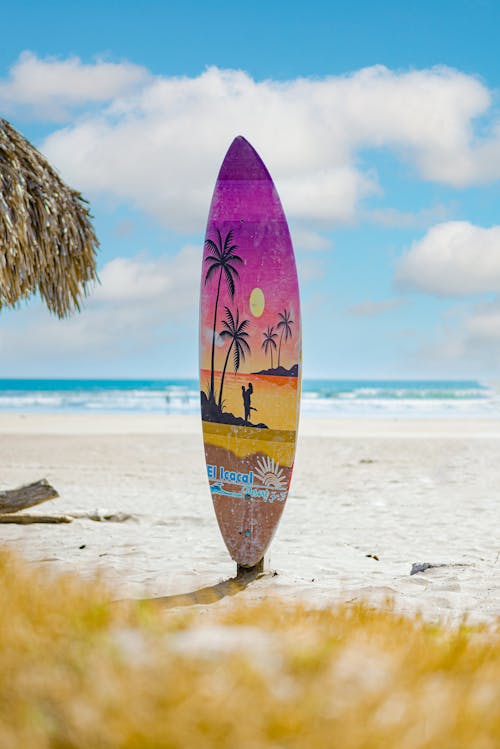 A Surfboard with a Painting Standing on a Beach 