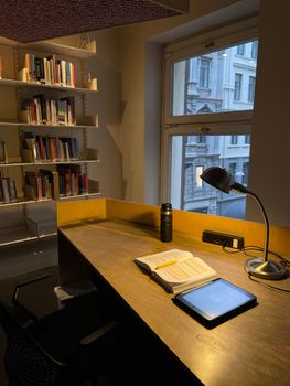 A warm and inviting desk setup with an open book, tablet, and lamp, perfect for studying or working.