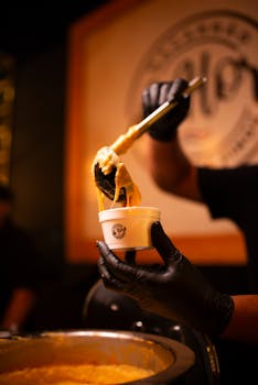 A vendor serves hot, cheesy mac and cheese in a cup at a food stall.