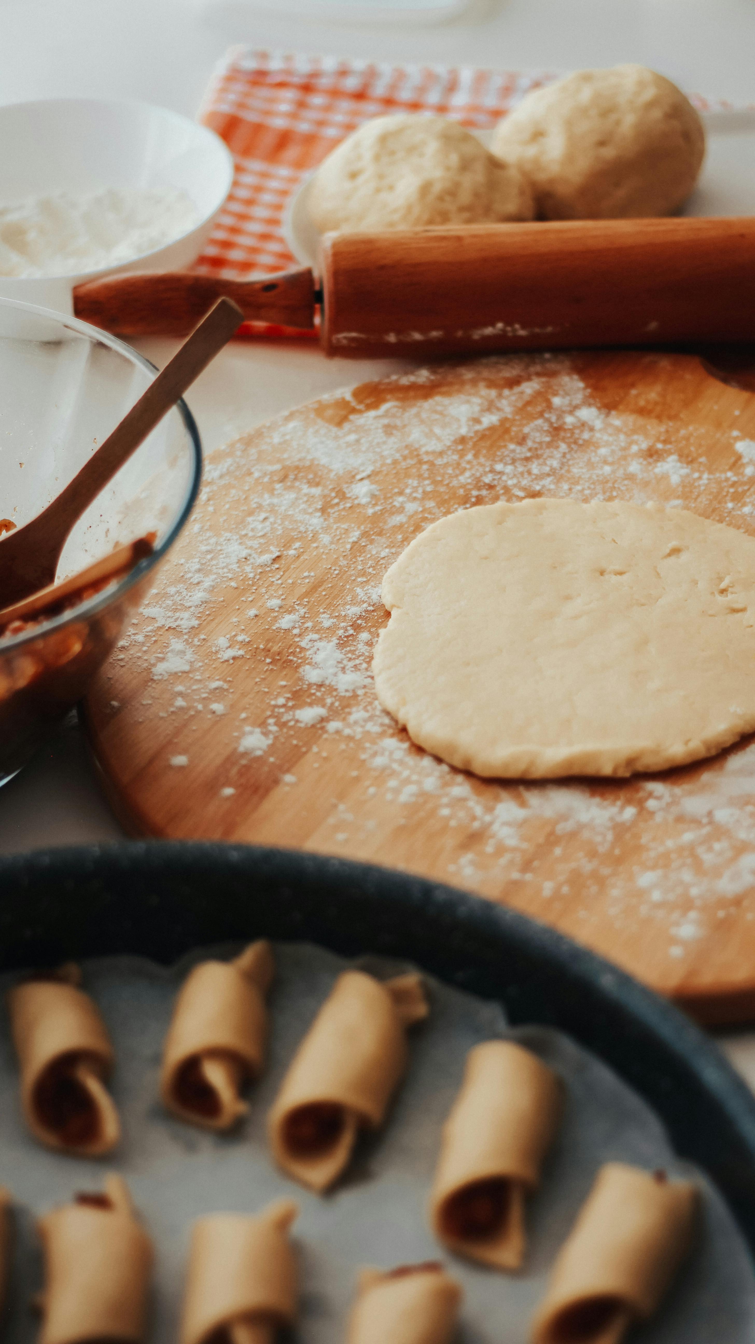 Close-up of dough preparation on a wooden board with rolling pin and baking tray.