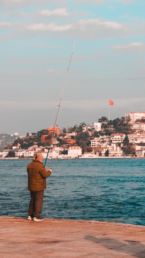 A man fishing on the water with a city in the background