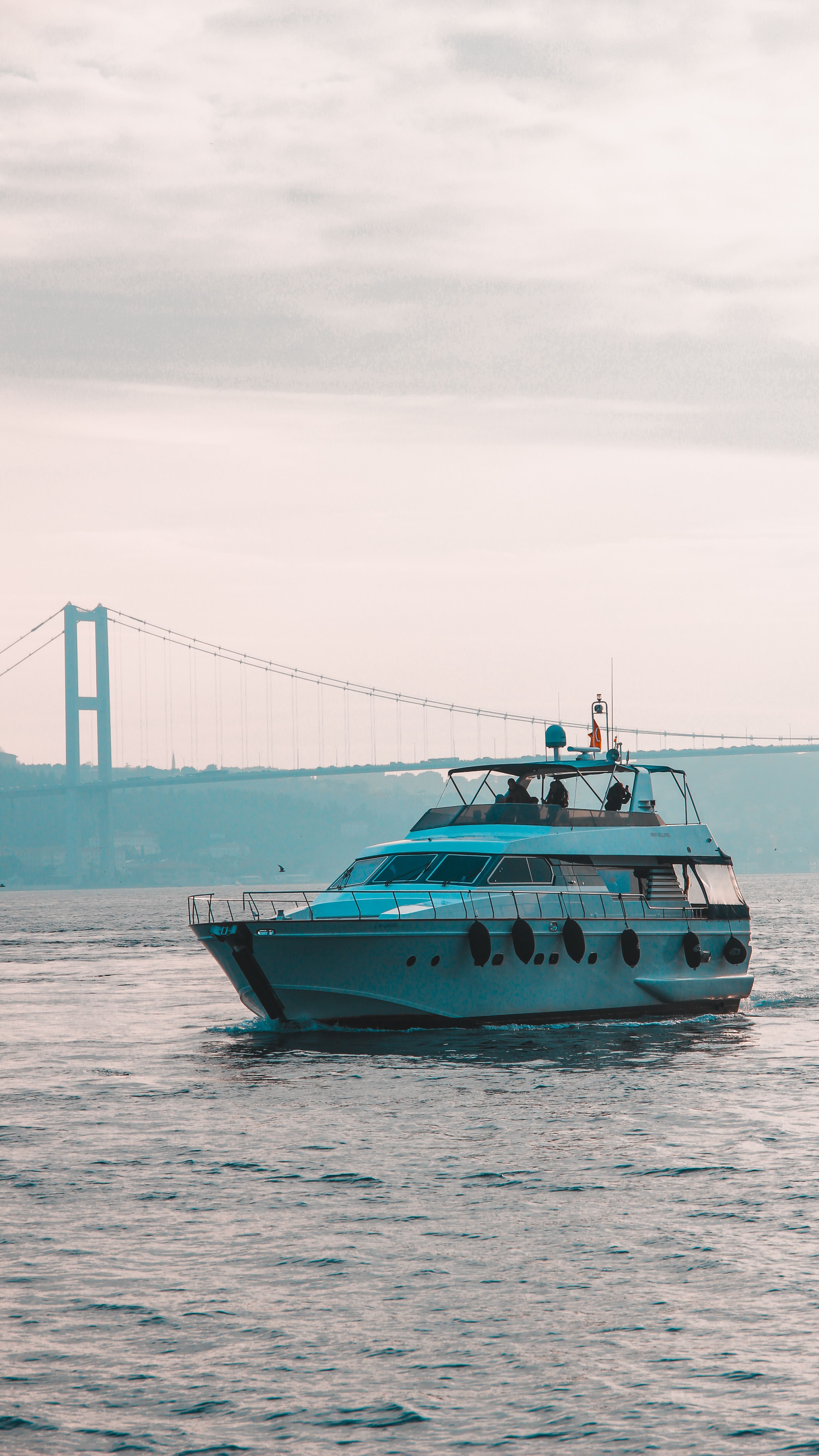 A luxury yacht cruising the Bosphorus with the iconic Istanbul bridge in the background.