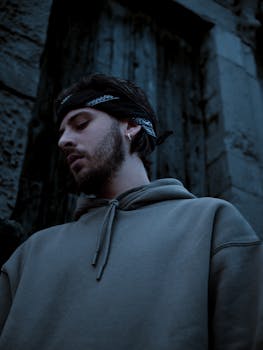 A moody portrait of a young man in a hoodie with a bandana, set against an urban backdrop.