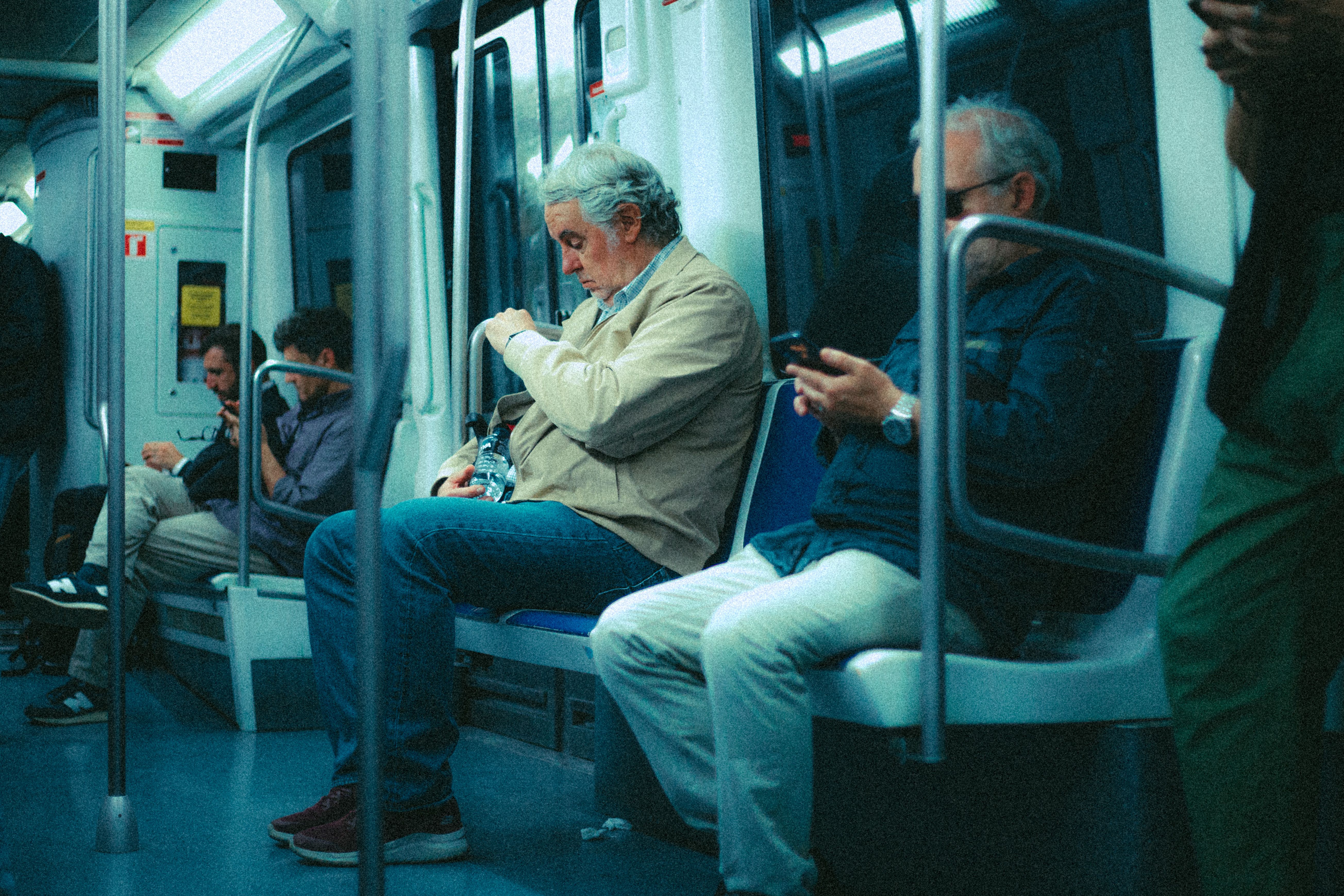 Senior adults commuting in a metro train, seated and using devices.