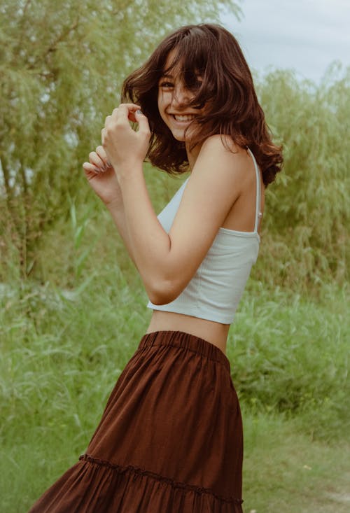 Young Woman in a White Top and Brown Skirt Standing on a Meadow 