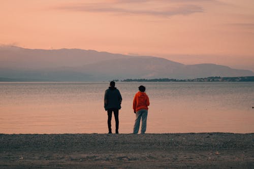 Two people standing on the beach looking at the water
