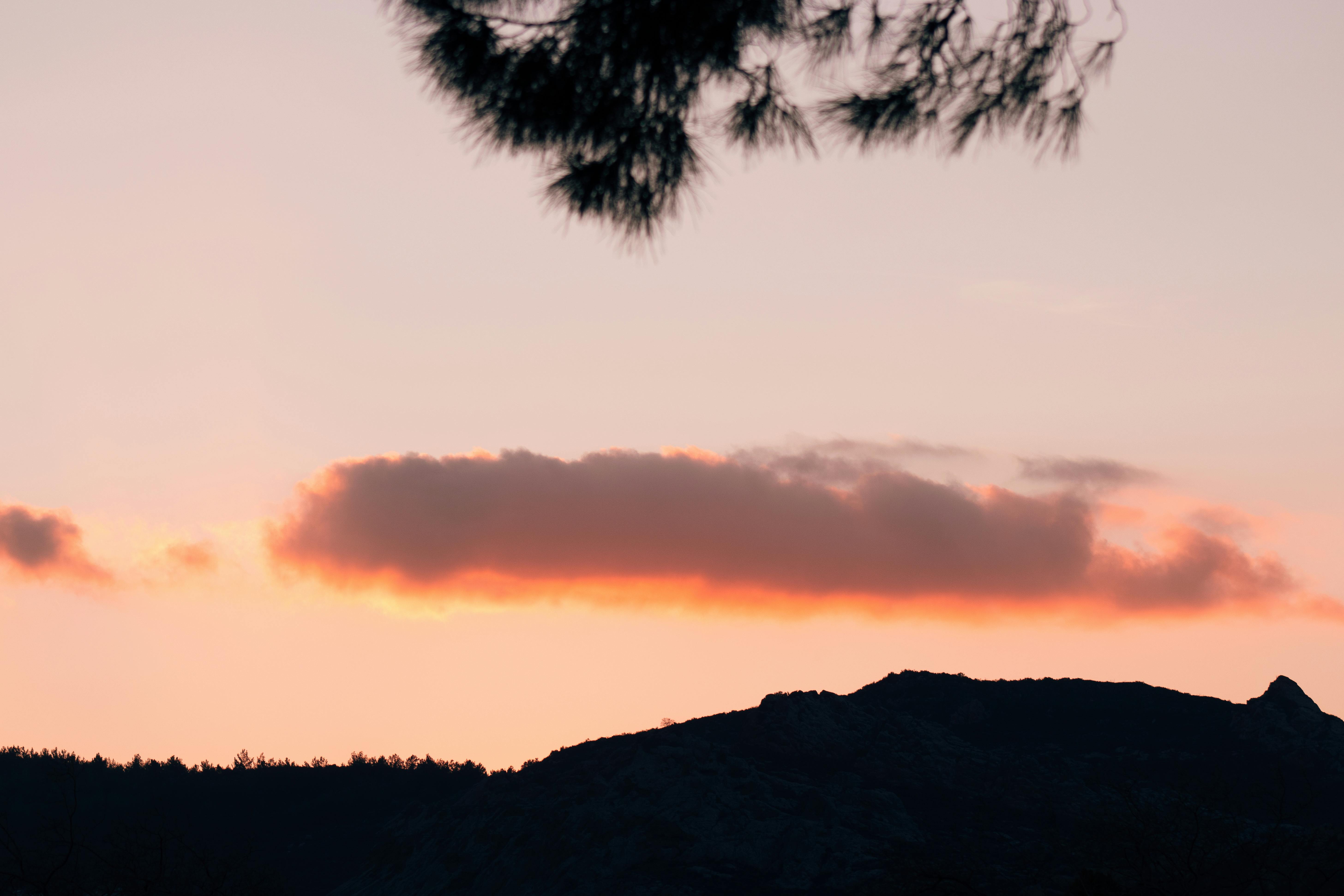 a sunset over a mountain with a cloud in the sky