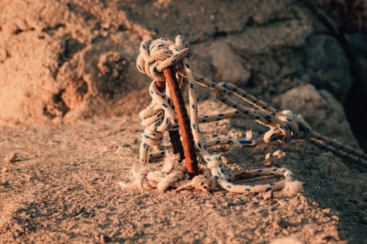 Close-up of a nautical rope tied to a rusty metal pole on a textured stone surface.