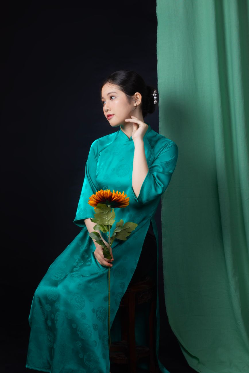 Elegant Asian woman in turquoise kimono posing with a sunflower against a dark backdrop.
