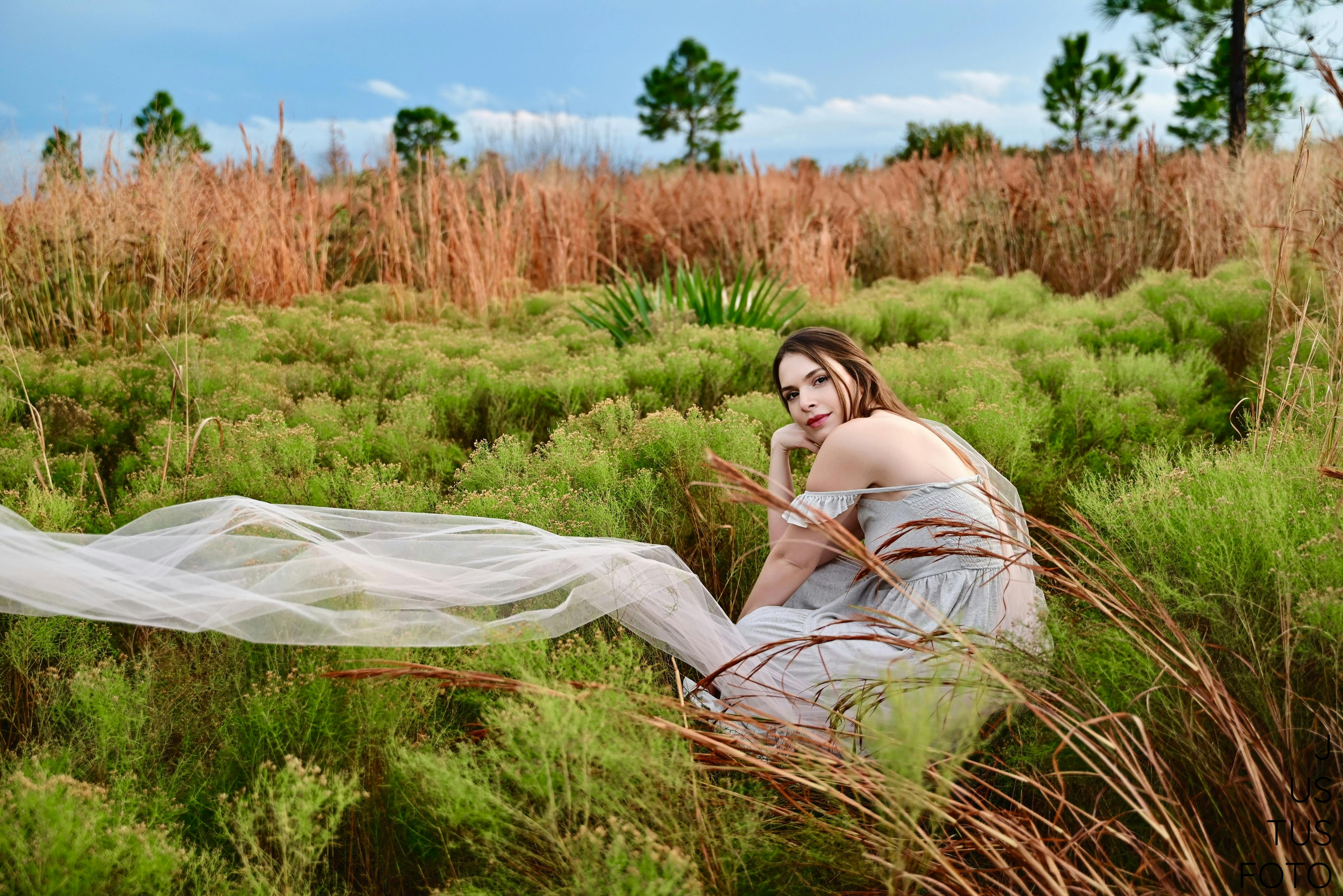 Elegant woman in a flowing dress sitting in the lush fields of Kissimmee, FL.