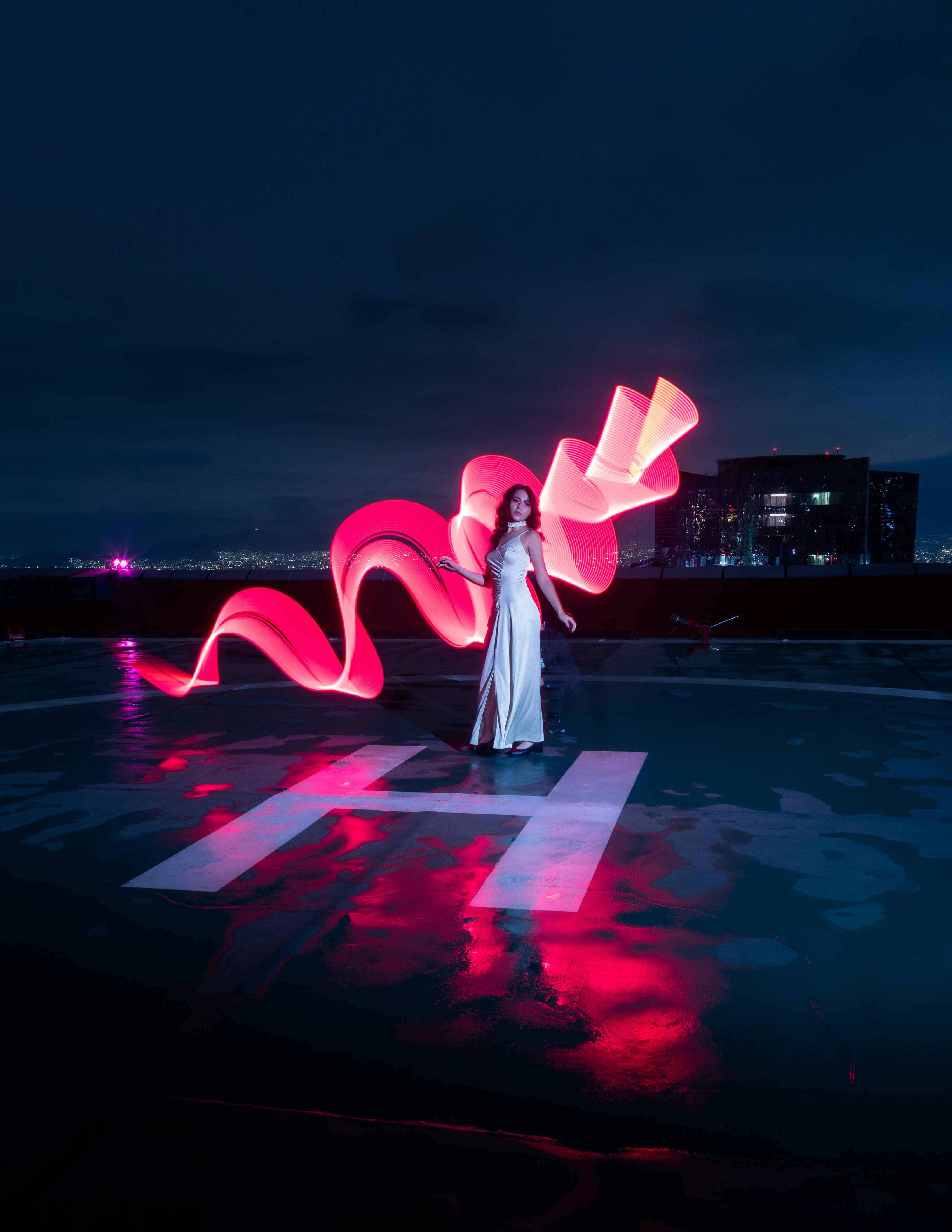 A glamorous nighttime scene of a woman elegantly posing with light painting on a rooftop in Mexico City.