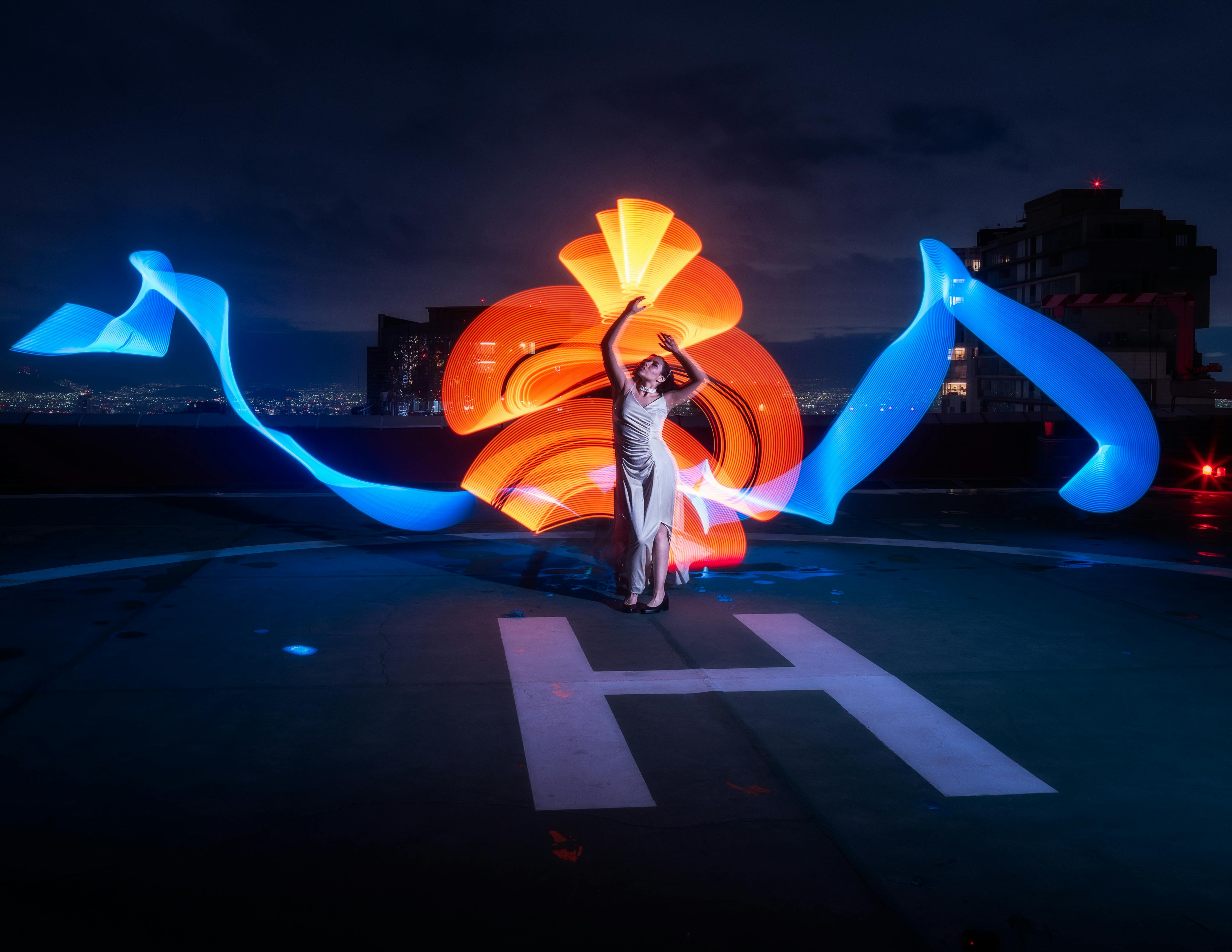 A woman in a striking white dress poses with dynamic light trails on a helipad in Mexico City at night.