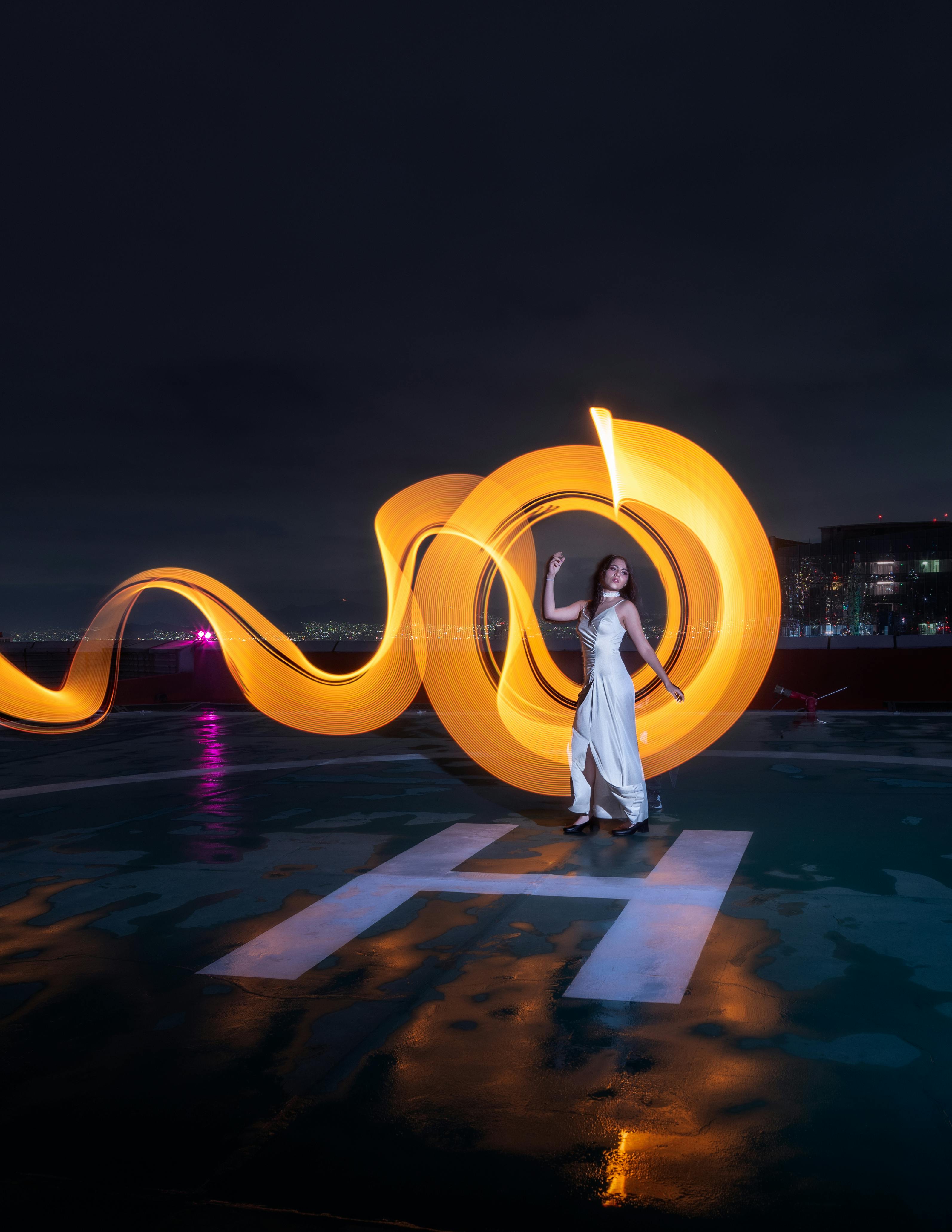 A woman in a white dress poses amidst neon light trails on a rooftop in Mexico City.