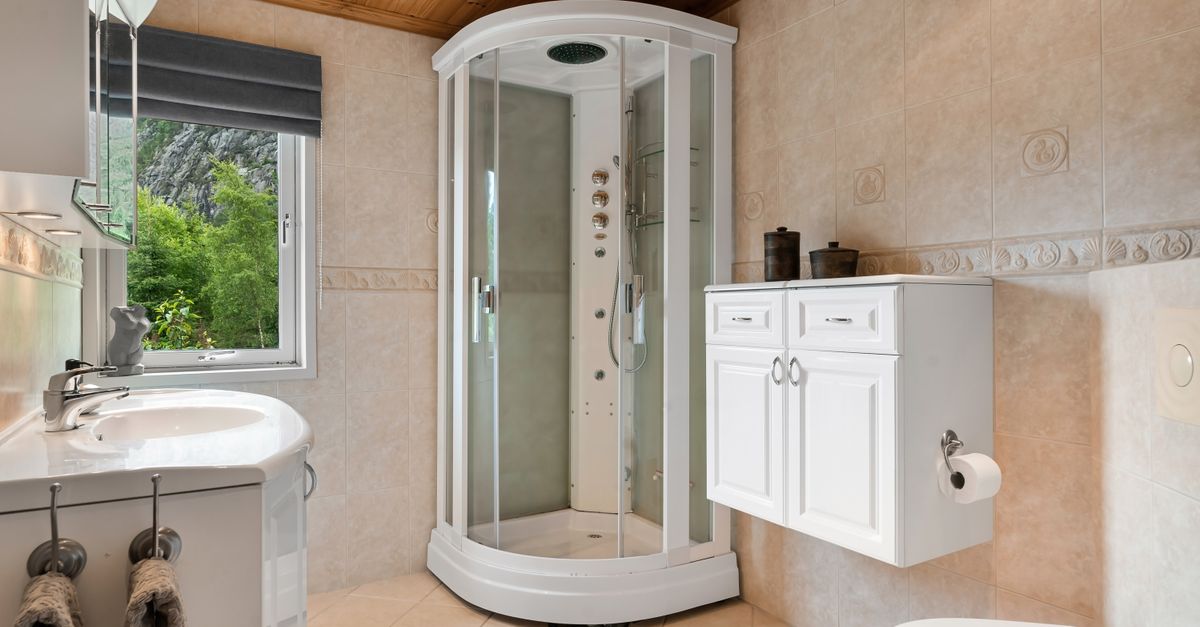 Bright and cozy bathroom featuring a glass shower, wooden ceiling, and a view of lush greenery through the window.