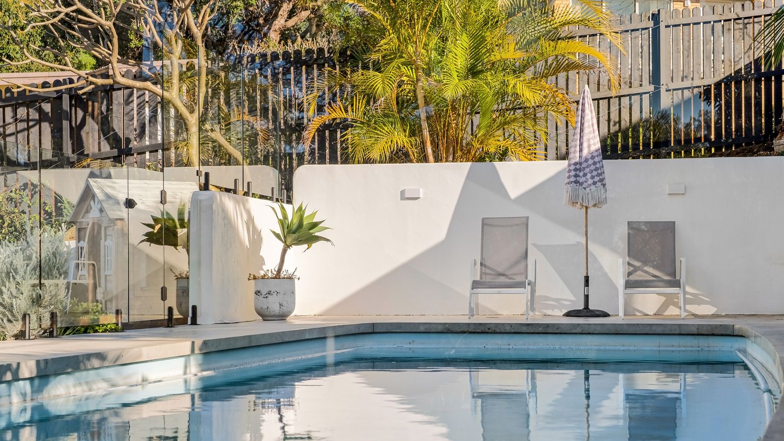Pool with a pale concrete surround and coping, rendered white walls and glass pool fencing