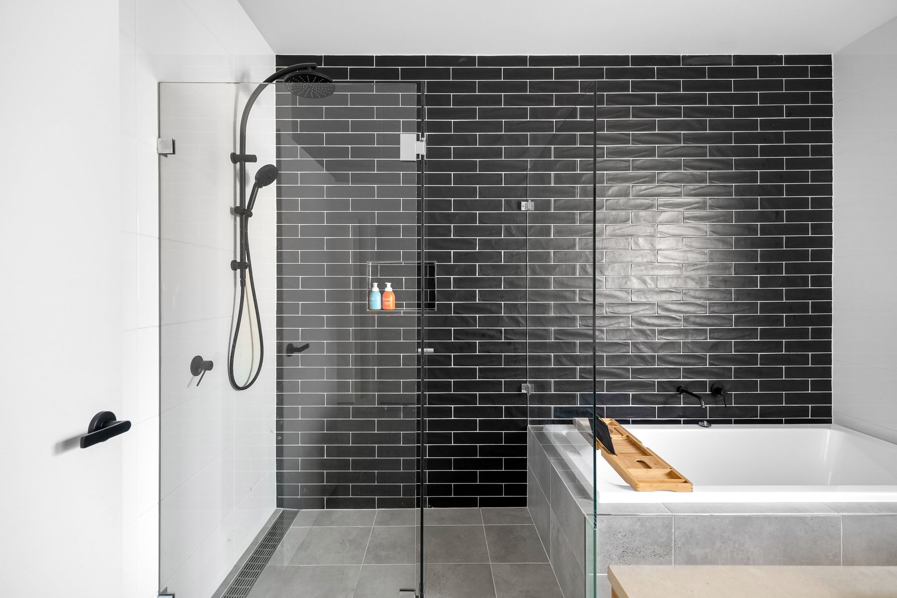 Dark tiled shower behind clear glass with restrained black fixtures