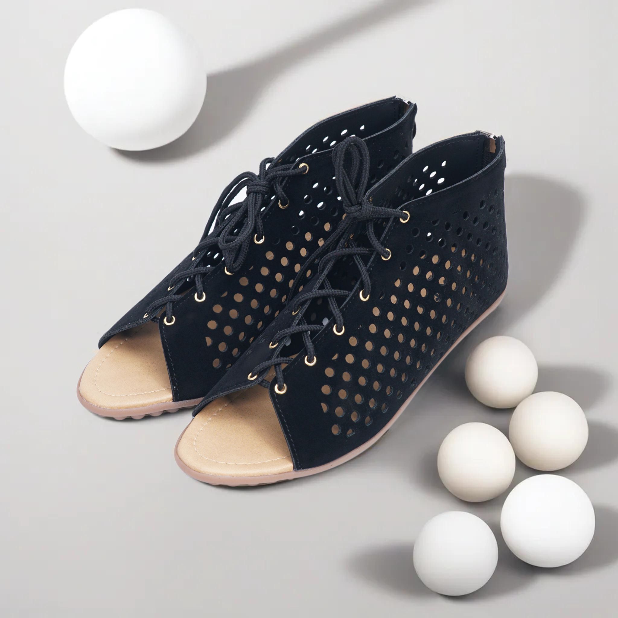 Elegant black open-toe sandals with perforated design against a minimalist studio background.