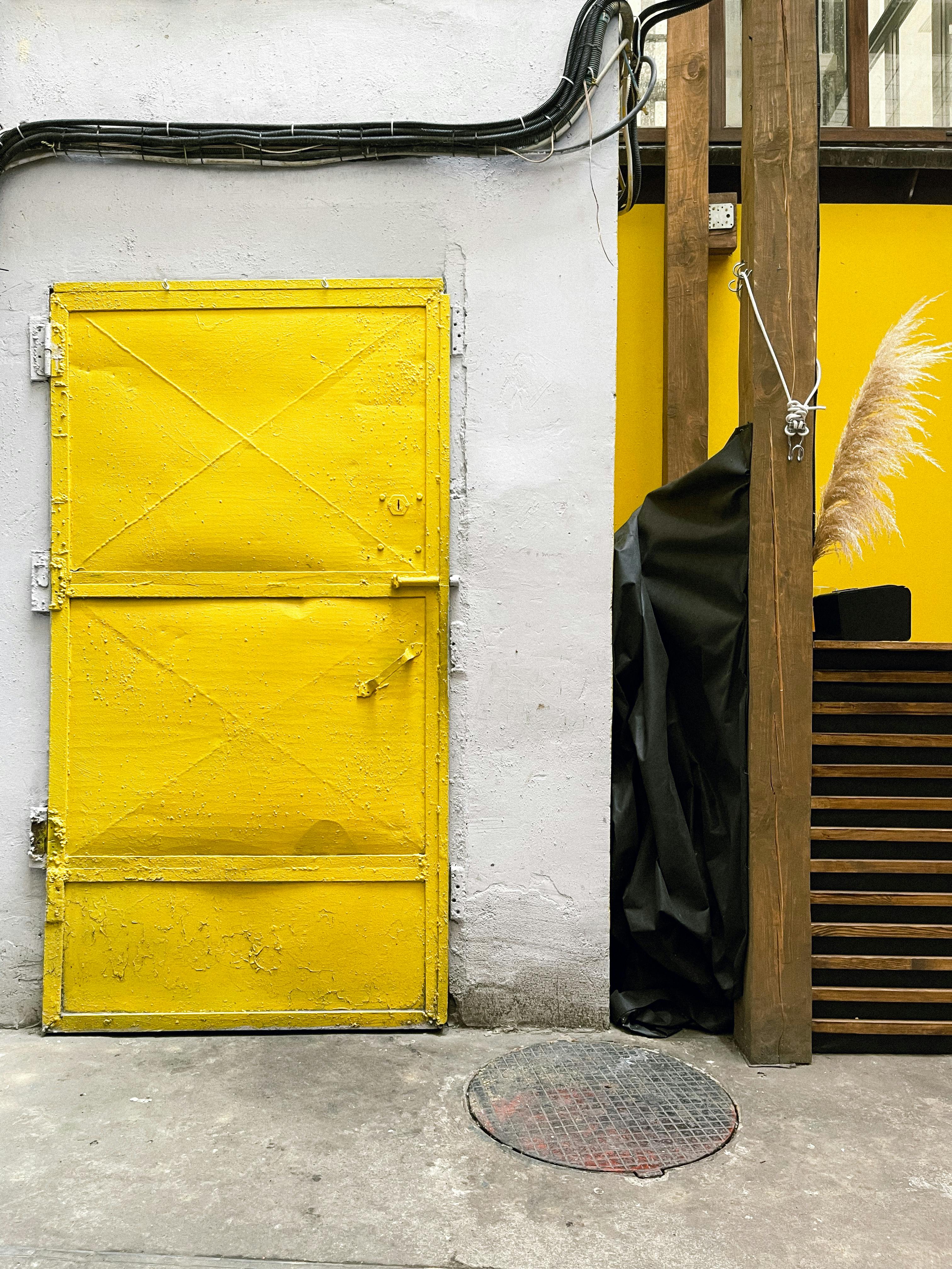 A striking yellow door against a concrete wall with urban elements and shadows.