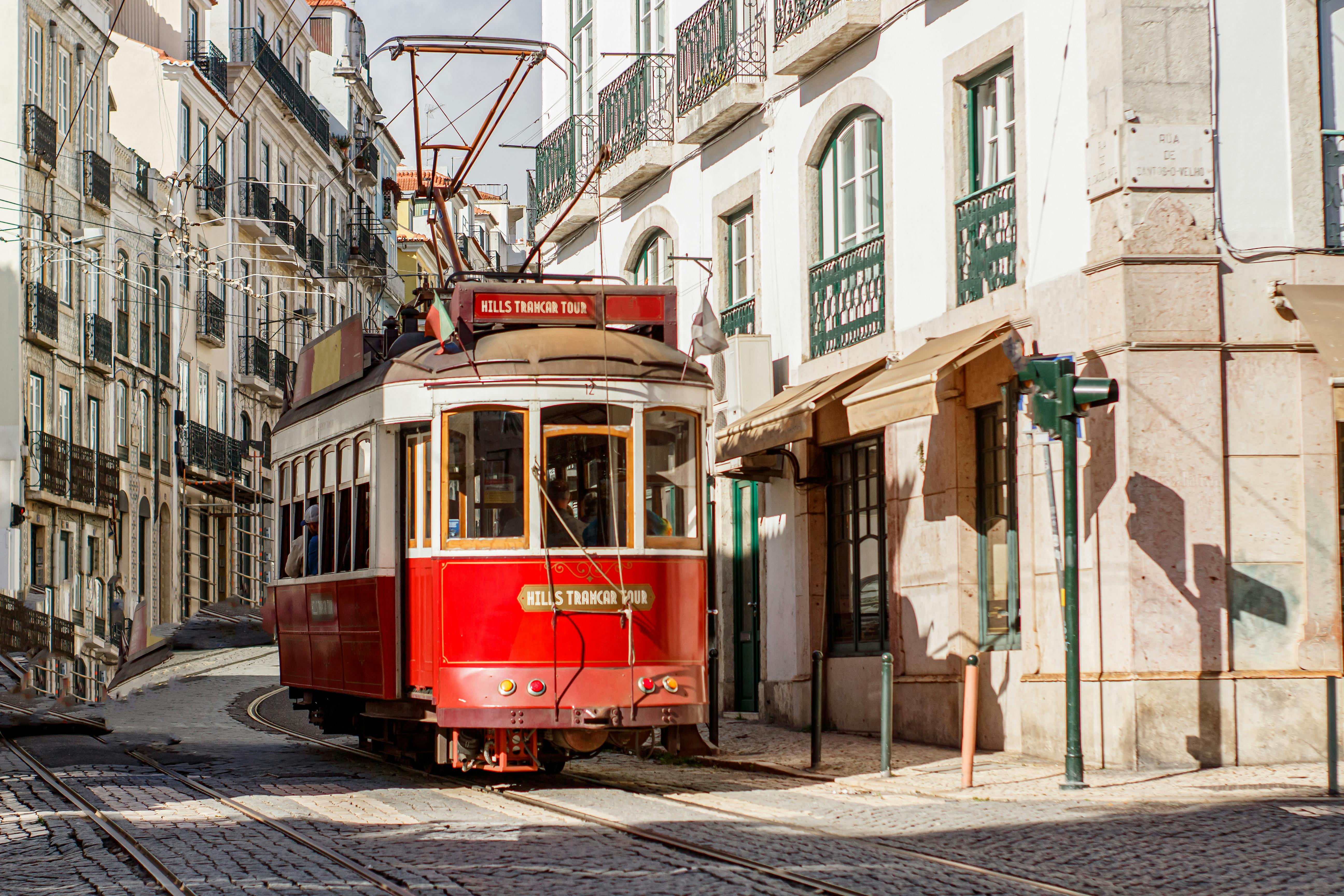 A classic red tram traverses the charming and narrow streets of Lisbon, Portugal, under the bright day sun.