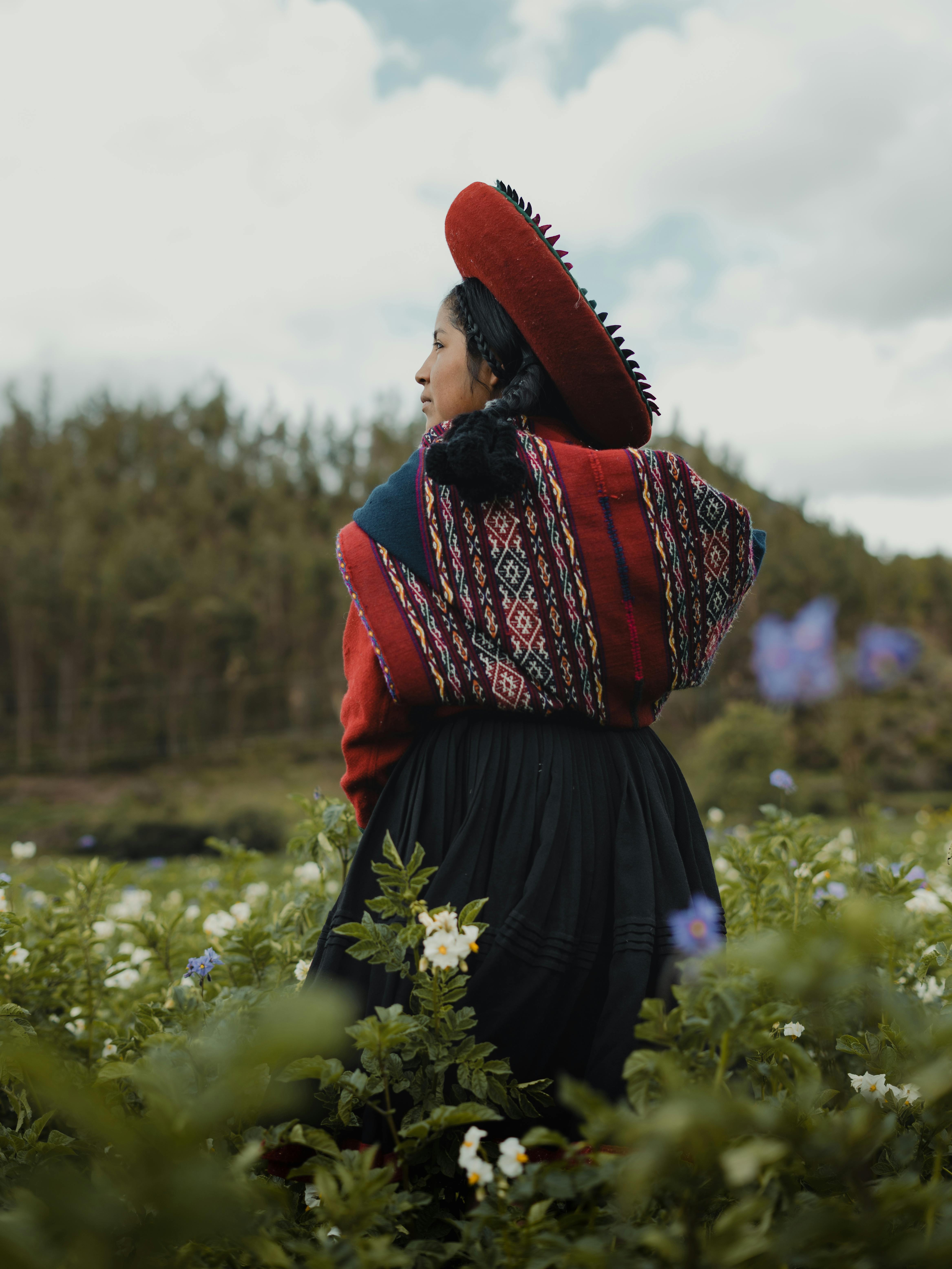 A woman in traditional Peruvian attire stands in a vibrant meadow near Cusco, Peru.