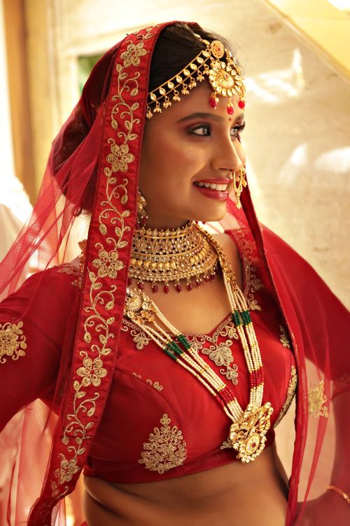 Free A beautiful Indian bride in ornate red attire with traditional jewelry, captured indoors. Stock Photo