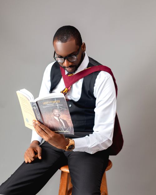 Free Man in formal attire reading a book while sitting on a stool in a studio setting. Stock Photo