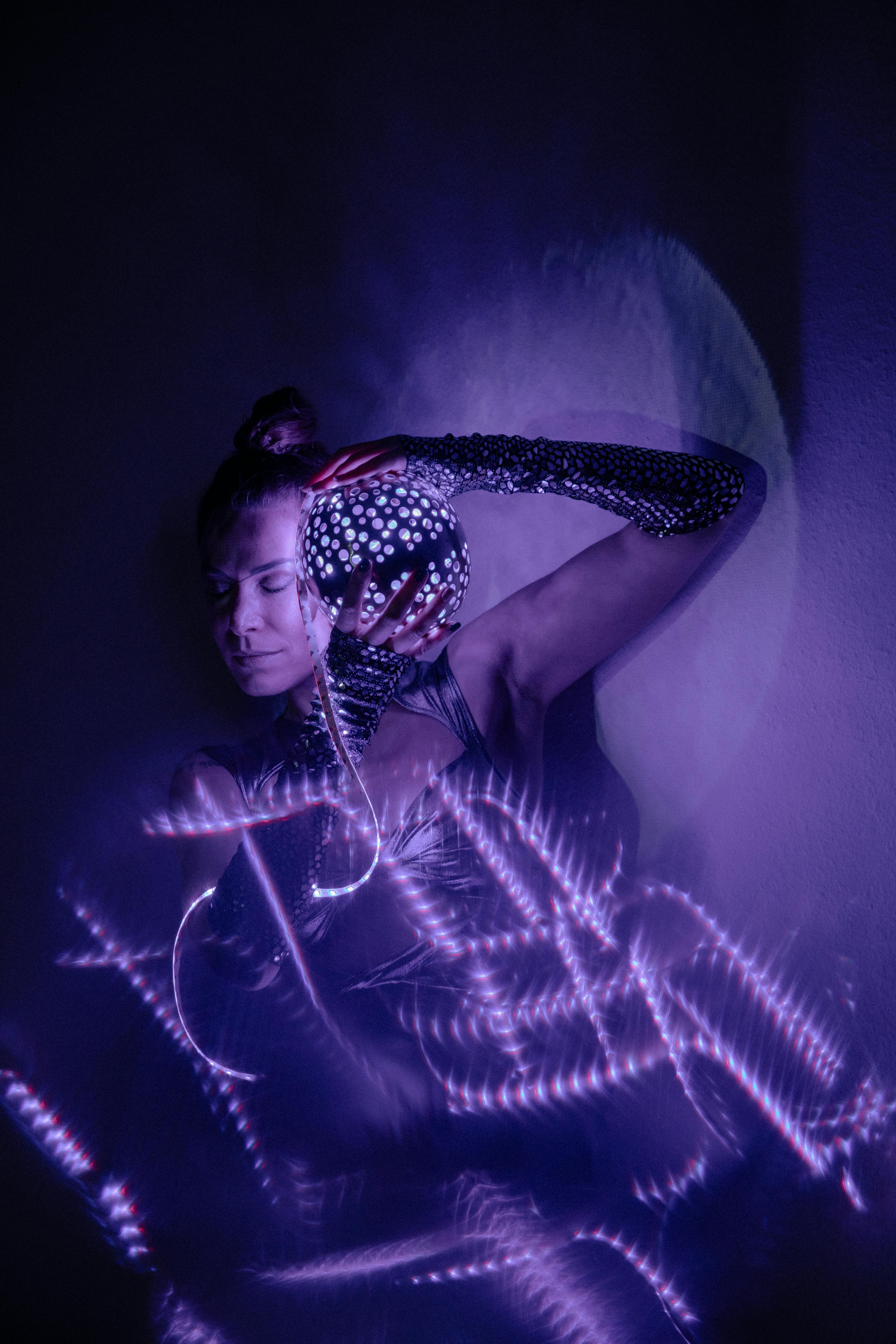 Artistic portrait of a woman with neon purple lights, eyes closed, and reflective accessories.