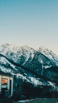 Charming village beneath snowy mountains during sunset, serene winter landscape.